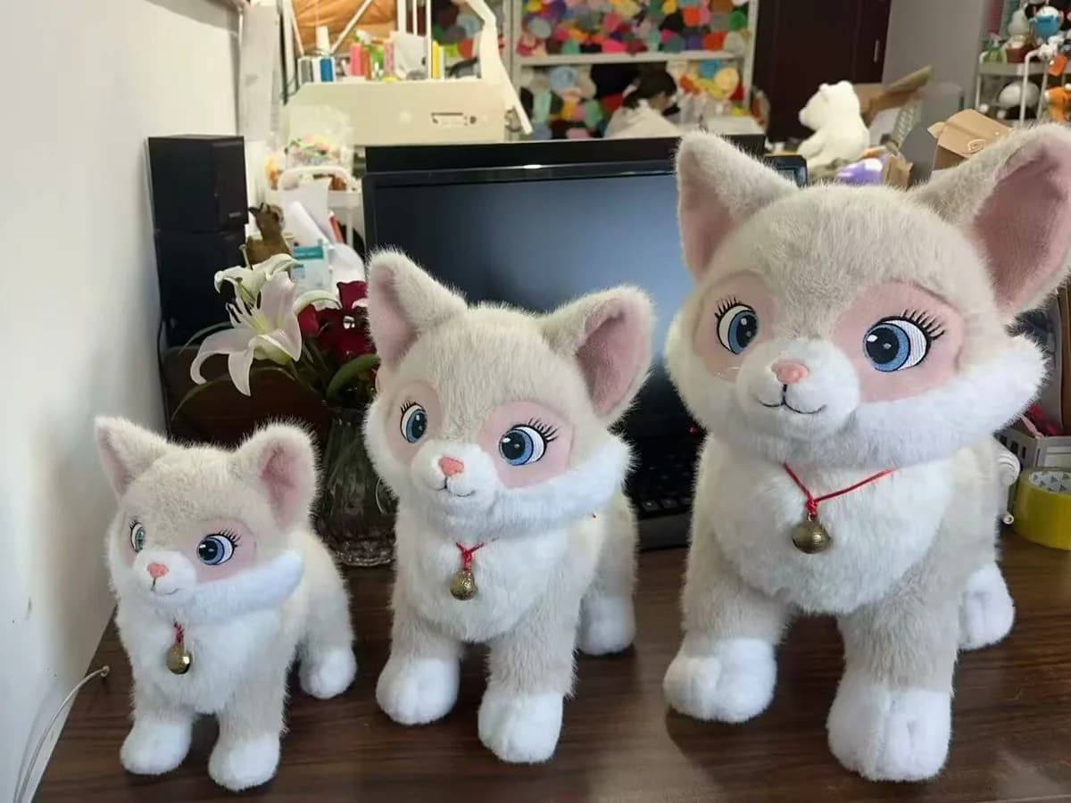 The same cat plush pattern sewn at three sizes, photographed on the sample bench