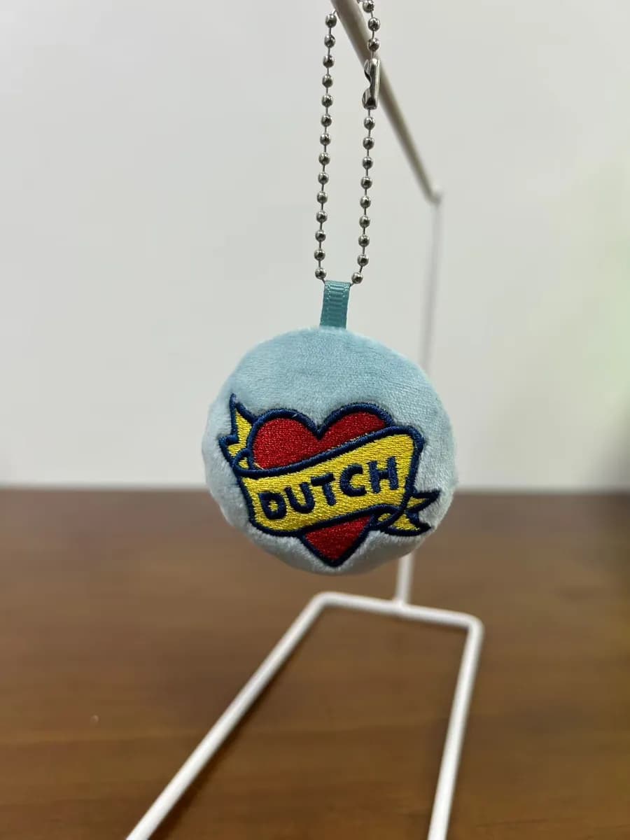 Round plush badge charm with a woven brand label